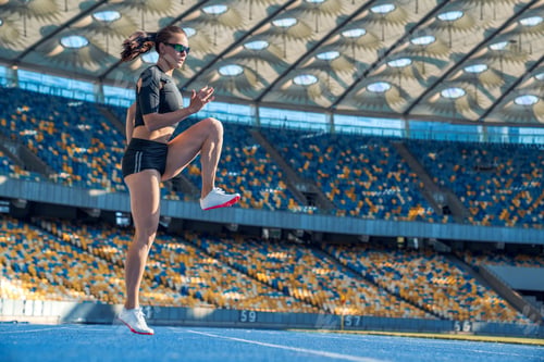 Preview: Young woman runner athlete stretching legs before run during sunny morning on stadium track