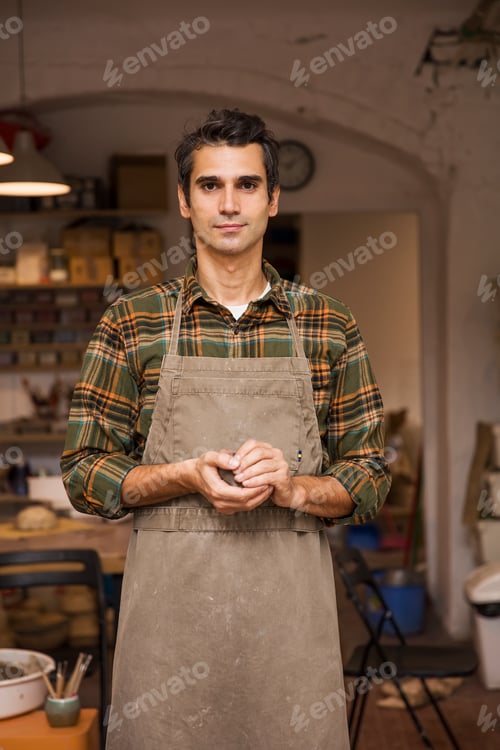 Preview: Handsome young man in pottery workshop holding clay