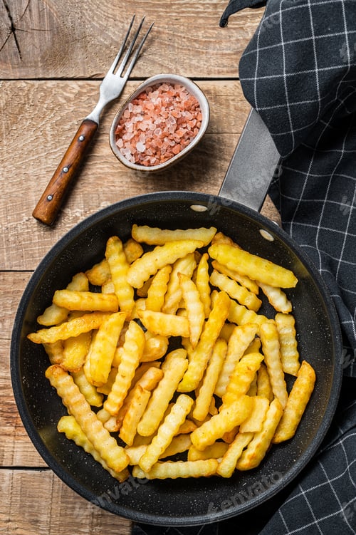 Preview: Deep fried Crinkle French fries potatoes sticks in a pan. Wooden background. Top view