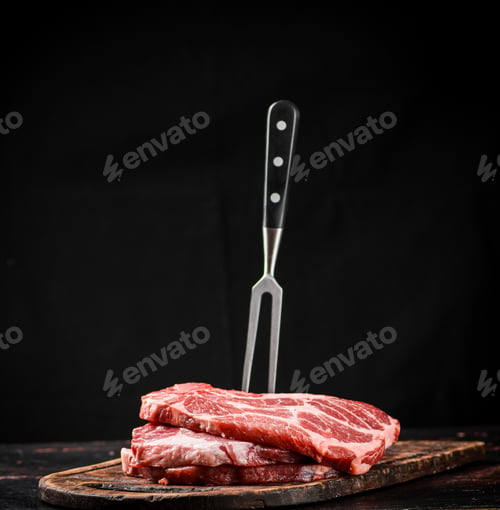 Preview: Raw pork steak on a cutting board with fork.