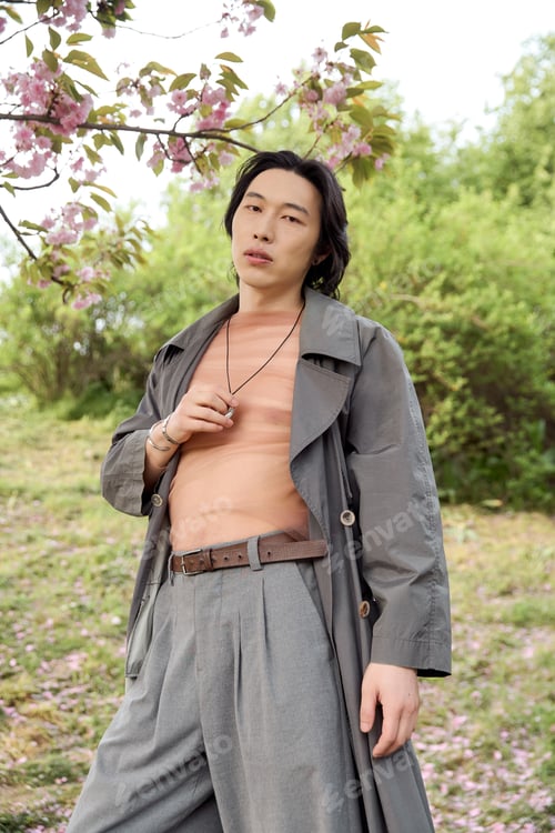 Preview: Stylish young man enjoys nature while displaying his modern grey outfit in a serene park
