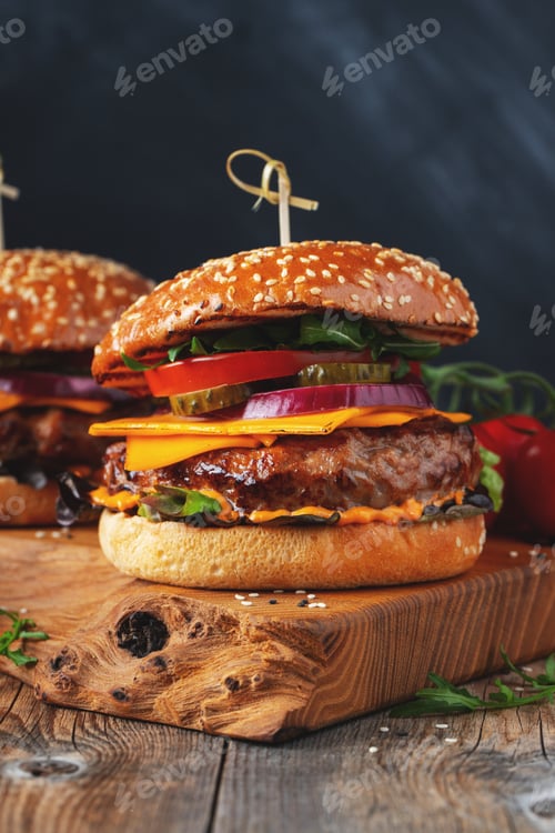 Preview: Two delicious homemade burgers of beef, cheese and vegetables on an old wooden table.