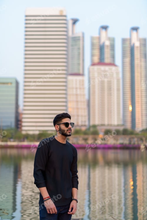 Preview: Young handsome Indian man thinking while wearing sunglasses agai