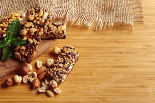 Preview: Snack bars with nuts and seeds placed on a wooden board next to scattered nuts and a mint leaf
