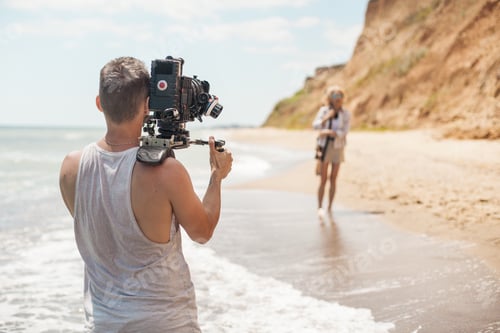 Preview: Professional videographer- film maker filming music clip on sand coast - beach near sea.