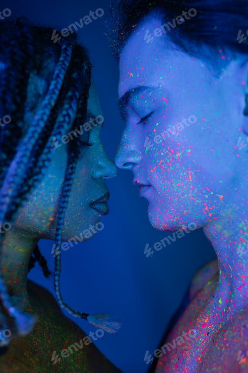 Preview: bare-chested interracial couple in colorful neon body paint standing face to face with closed eyes