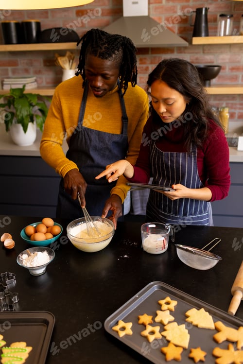 Preview: Happy diverse couple baking christmas cookies using tablet in kitchen, copy space