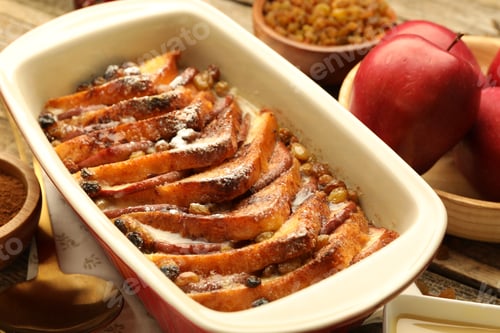 Preview: Freshly baked bread pudding in baking dish and apples on table, closeup