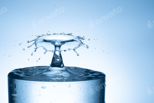 Preview: Water drop splashing into glass from isolated bright background.