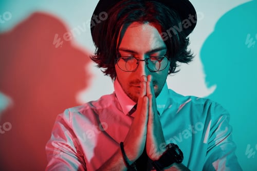 Preview: Portrait of young stylish man in hat and with glasses that stands in neon lights in the studio