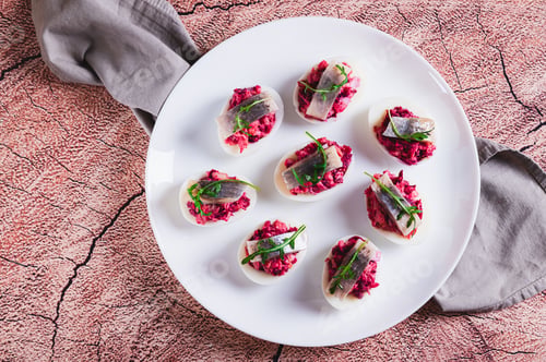 Preview: Close up of egg halves stuffed with herring under a fur coat on a plate on the table top view