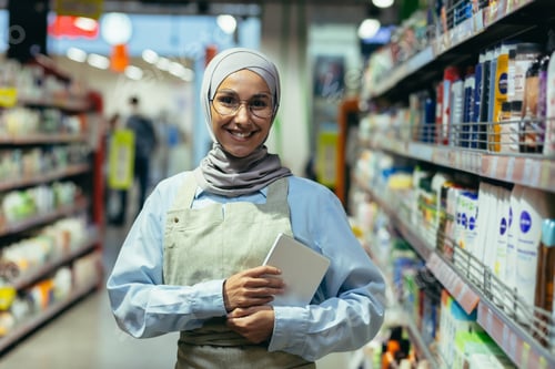 Preview: Portrait of a woman in a hijab, a shop worker in a supermarket with a tablet computer, looks at the
