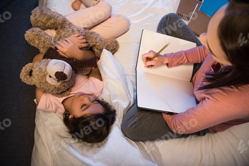 Preview: selective focus of daughter with teddy bear sleeping while mother working at night