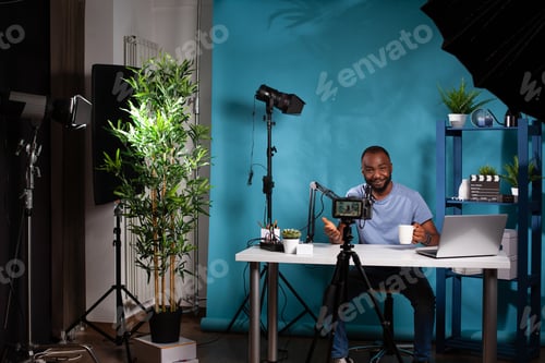 Preview: Content creator talking to followers in in front of filming video camera on tripod sitting at desk