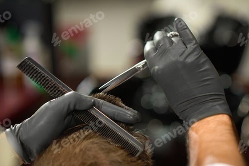Preview: Closeup of hands of barber in protective gloves cutting hair