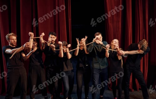 Preview: Knot in the hands. Group of actors in dark colored clothes on rehearsal in the theater