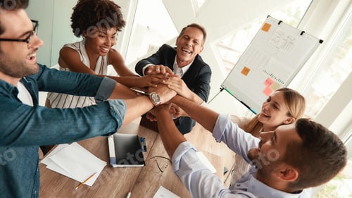 Preview: Happy business people holding hands together while sitting at the office table