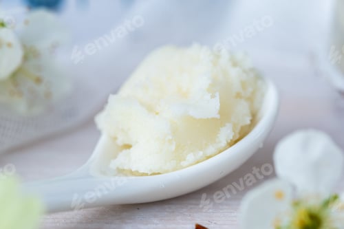 Preview: Selective focus shot of a spoonful of shea butter and some white flowers on a white table top