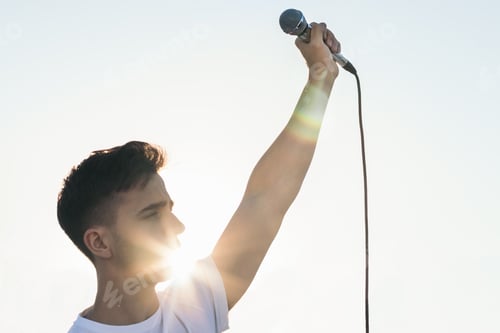 Preview: singer with the arm raised holding a microphone with sunlight reflects