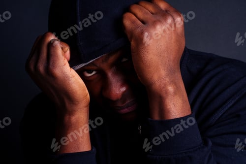 Preview: worried young african american mele wearing gray hat and black hoody with hood