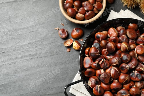 Preview: Delicious roasted edible chestnuts on black slate table, flat lay. Space for text