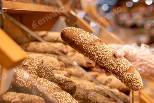 Preview: Gloved hand of female buyer holding fresh bread sprinkled with sesame seeds