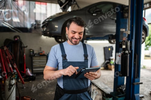 Preview: Car mechanic using a tablet in a workshop with a lifted car