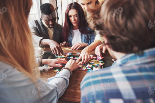 Preview: Group of creative friends sitting at wooden table. People having fun while playing board game