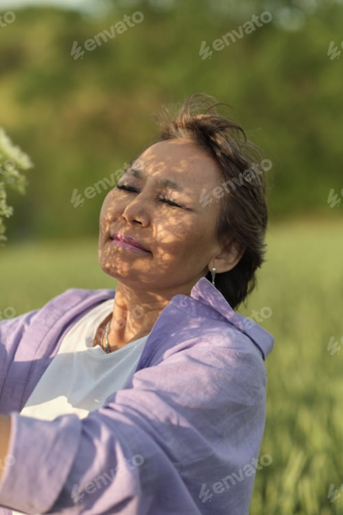Preview: smiling Asian woman of older age in a summer park, holding wild flowers. The video conveys an