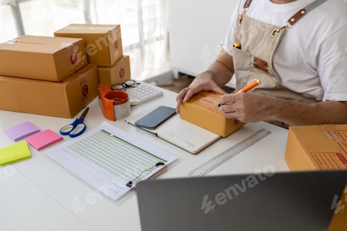 Preview: Person writing a customer's address on a parcel box, selling products online, packing orders from cu