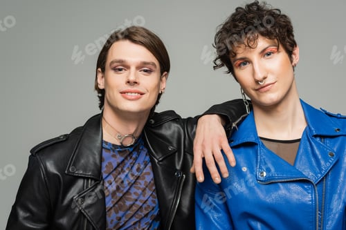 Preview: carefree pansexual partners in leather jackets and makeup looking at camera isolated on grey