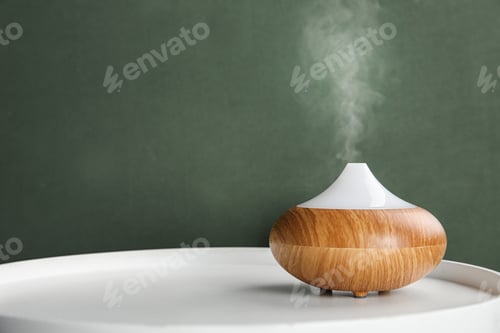 Preview: Modern essential oil diffuser on white table against green background. Space for text