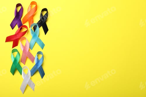 Preview: Colorful ribbons on yellow background, flat lay with space for text. World Cancer Day