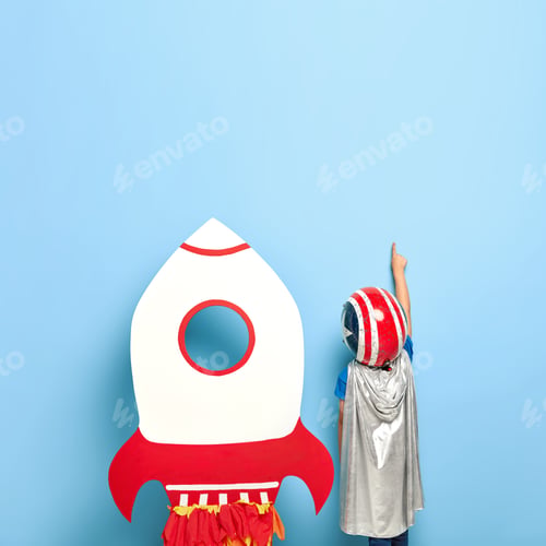 Preview: Faceless unrecognizable child stands back to camera, wears helmet and grey cape, points index finger