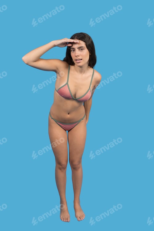Preview: Young woman in pink bikini shielding eyes while searching on blue background