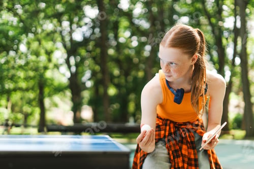 Preview: Red hair girl playing ping pong outdoors on summer day