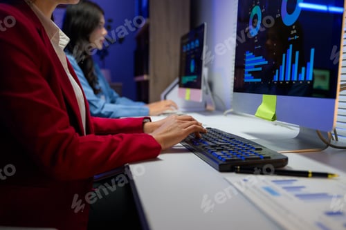 Preview: Office workers using computers with graphs and charts displayed on screen, working late at night