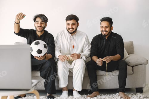 Preview: Three indian men sitting on a coach and watching football on laptop