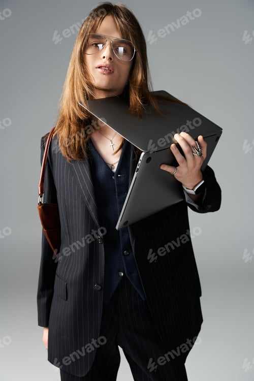Preview: A young man confidently poses in trendy attire, balancing a laptop with effortless style