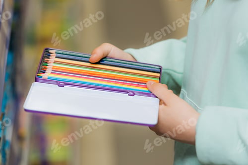 Preview: partial view of child holding set of new color pencils