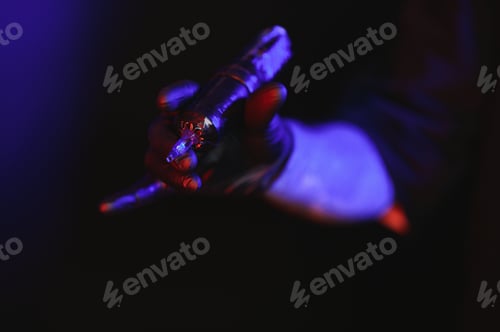 Preview: Gloved Hand Holding Tattoo Gun in Blue Light