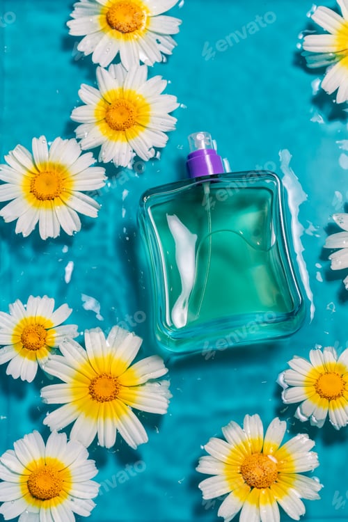 Preview: Vertical shot of a perfume bottle on water with daisies against a blue background with copy space