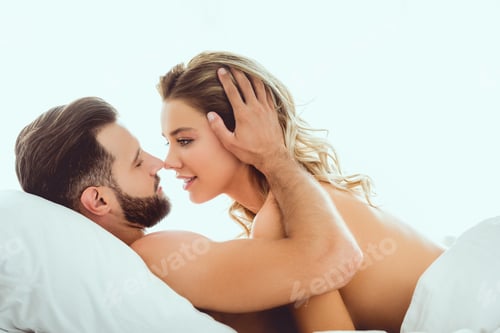 Preview: happy young couple embracing and looking at each other while lying in bed