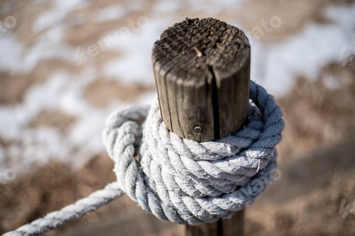 Preview: Close-up shot of a white rope tied securely to a brown wooden pillar against a blurred background