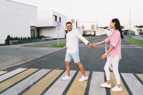 Preview: Happy diverse couple holding hands and walking on zebra crossing in street