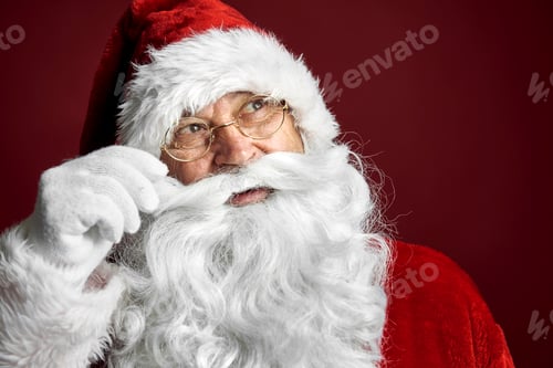 Preview: Smiling caucasian Santa Claus touching mustache on red background