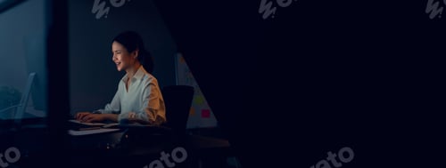 Preview: Smiling Asian business woman sitting the table and working on computer in office at night