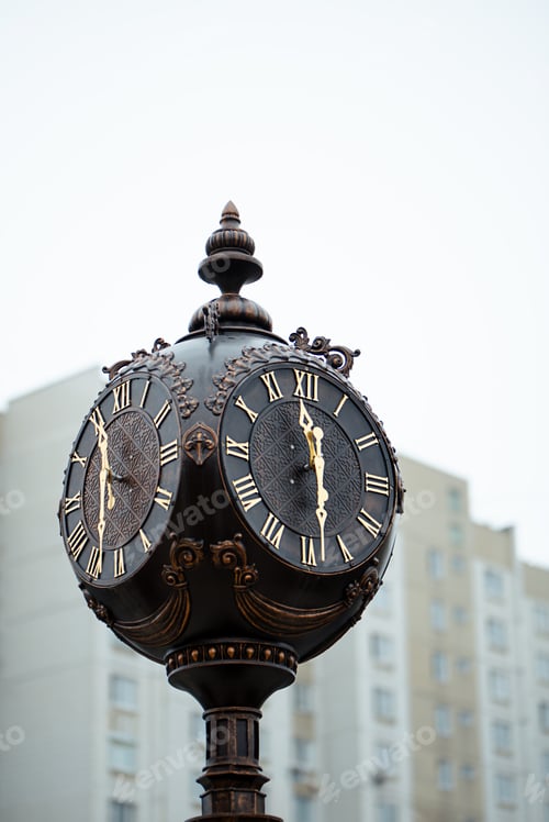 Preview: Street metal brown clock with Roman numerals close-up on the background of the house.