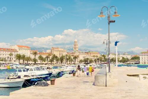 Preview: Sunny day at a Mediterranean marina with boats docked, people strolling, and historic