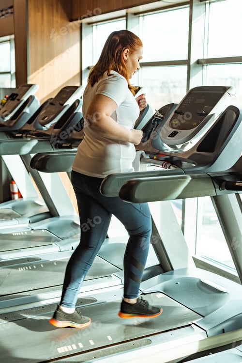 Preview: overweight girl working out on treadmill in gym near window